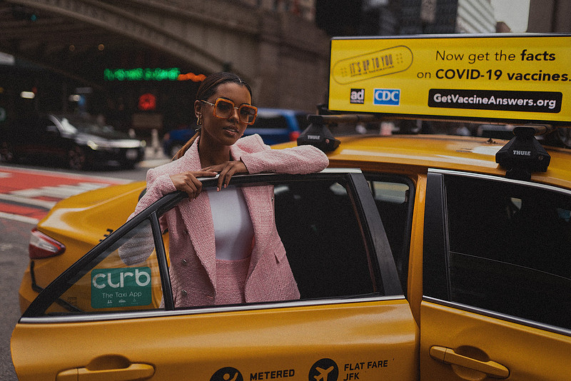 Selena Jutton framed by midtown textures as a yellow cab approaches the curb.