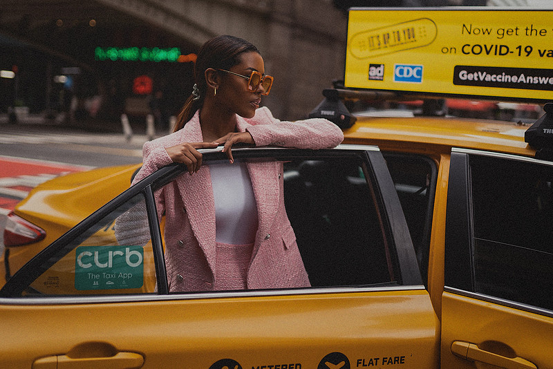 Selena Jutton walks along a Midtown block in a blush pink suit, traffic and scaffolding behind her.
