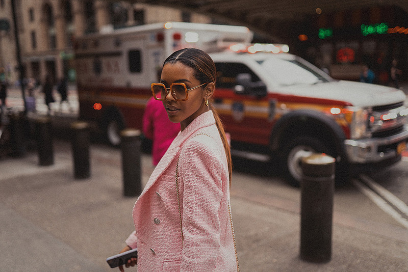 Selena Jutton rests her hands on the roof of a New York taxi as traffic passes in soft blur.