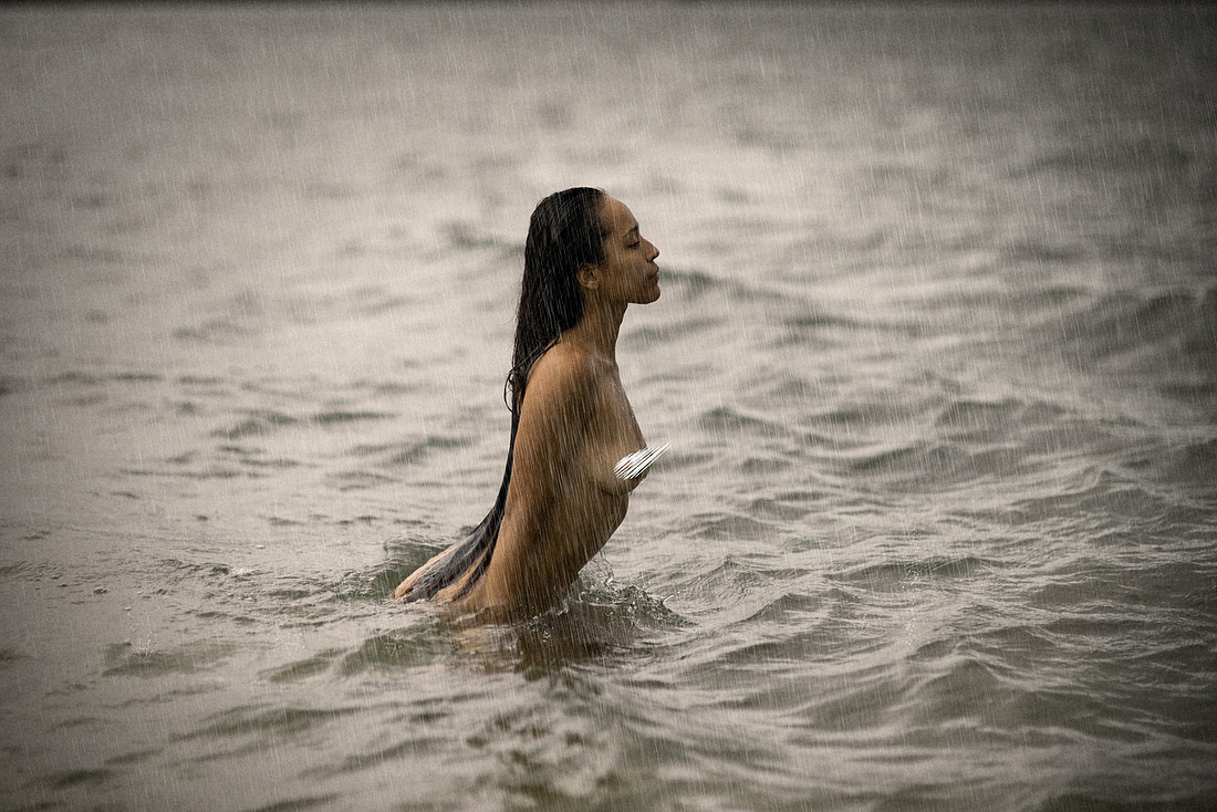 Back view of Becky Deeve standing in the rain; her spine arches slightly as she faces the storm, water running down her back and thighs.