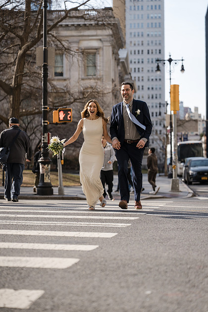 Newlyweds running across a downtown crosswalk, bride holding a bouquet — joyful NYC City Hall moment