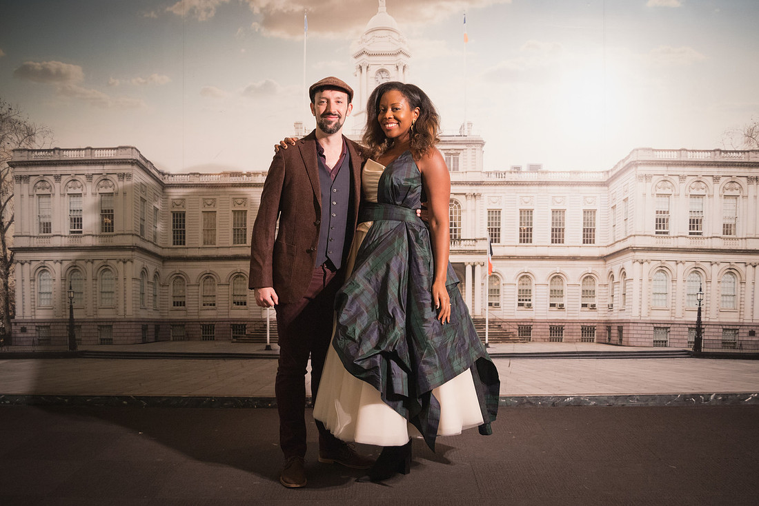 Smiling couple standing before the NYC City Hall backdrop inside the Manhattan Marriage Bureau, formal attire, soft indoor light.