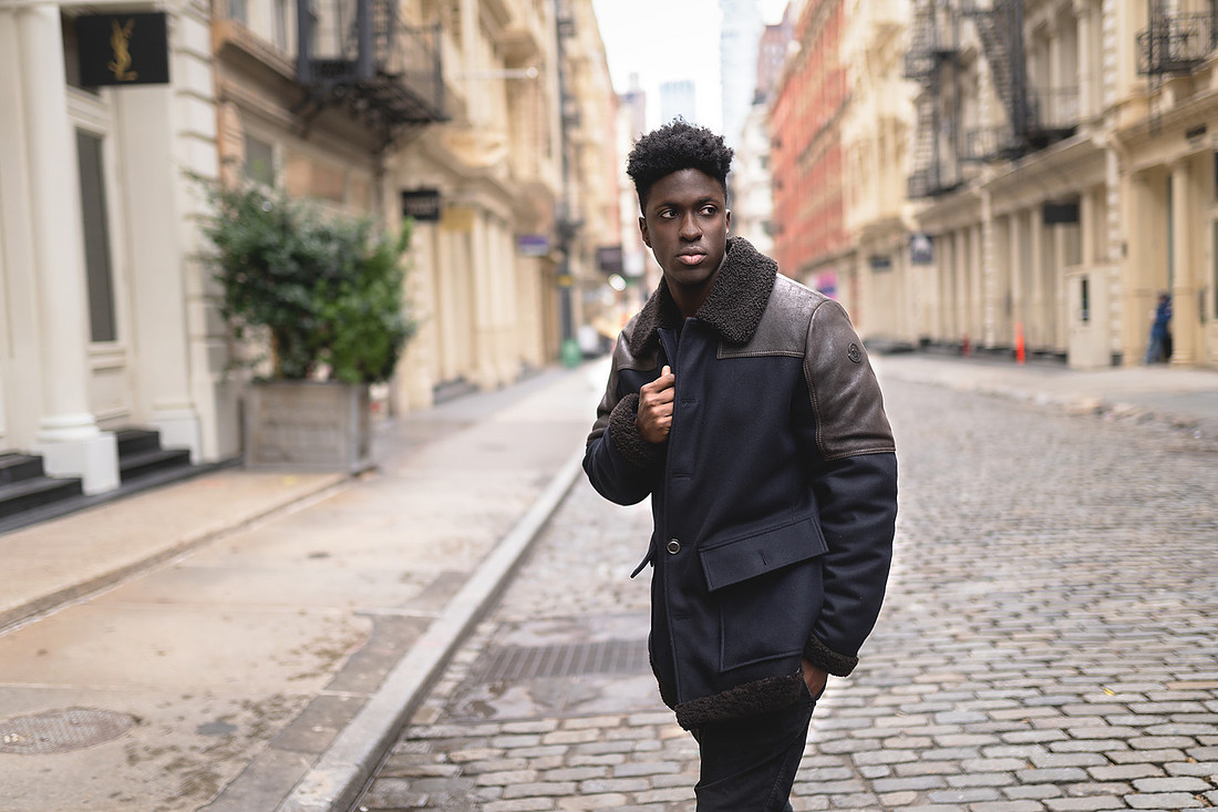 Solo portrait of Marvin Bienne on a SoHo street wearing a vintage Moncler shearling‑collar jacket and dark denim.