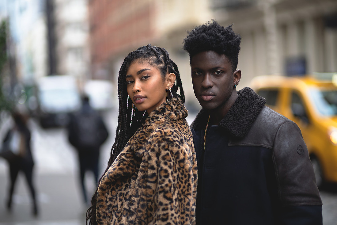 Jasmine Blandford walks ahead in a leopard coat and knee‑high studded boots while Marvin Bienne follows in a vintage Moncler jacket on a SoHo cobblestone street.