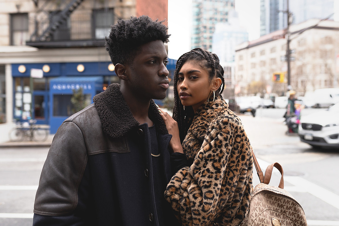 Marvin Bienne and Jasmine Blandford walk together on cobblestones; she wears a leopard‑print coat and he wears a shearling‑collar vintage Moncler jacket.